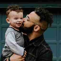 Image of a dad, holding his toddler and giving him a kiss on the cheek