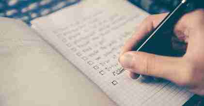 ADHD Essentials: 8 Therapist-Guided Tips for Thriving with Your ADHD Brain 7 A hand is writing with a pen on a gridded notepad, checking off tasks in a casual setting. This organized checklist serves as an ADHD Essentials tool, helping bring clarity to the chaos of daily routines.