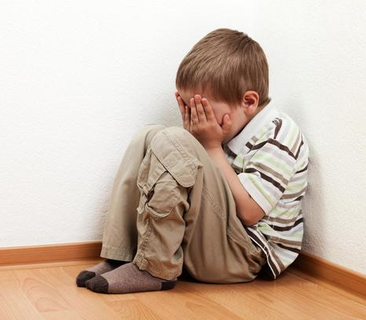 Image of a young boy sitting in the corner of a room with his face in his hands.