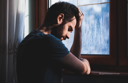Image of sad man, holding head facing a window