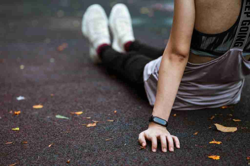 Sitting on the track in athletic wear, the person extends their legs, showcasing a fitness tracker subtly hinting at AI mental health support. With scattered leaves surrounding them, they exude calmness and balance fostered by therapist-approved AI to support executive functioning.