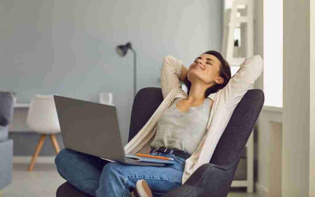 A woman sits in a chair with a laptop on her lap, leaning back with her hands behind her head and smiling—she looks relaxed, like a PMHN reviewing an ADHD diagnosis Ontario report in a bright, modern room.