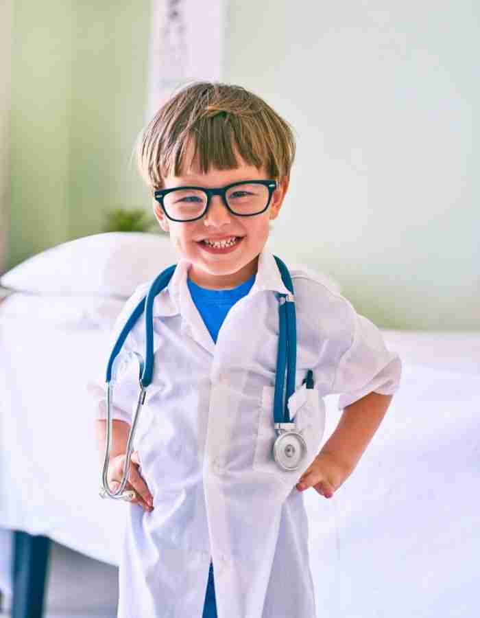 A young child wearing glasses and a white lab coat with a stethoscope around their neck smiles confidently, embodying the spirit of High Achievers with ADHD in a bright, medical-looking room.