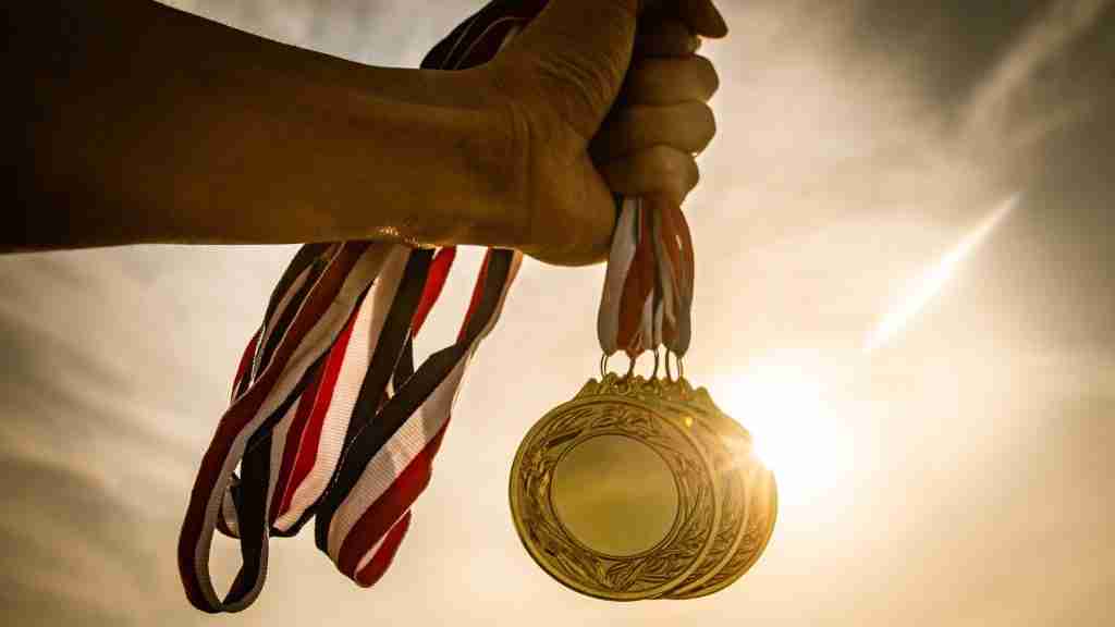 A hand holds up several gold medals with red, white, and blue ribbons against a bright, sunlit sky—celebrating High Achievers with ADHD mental health.