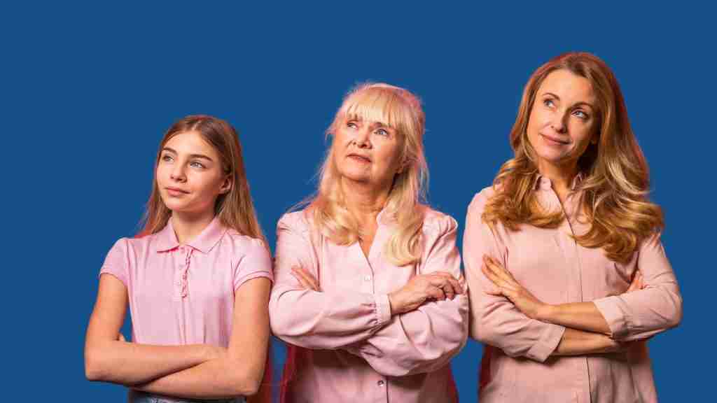 Three women of different ages—a young girl, an older woman, and a middle-aged woman—stand side by side with arms crossed in pink shirts, looking thoughtfully upward against a blue background, symbolizing generational stress in neurodivergent families.
