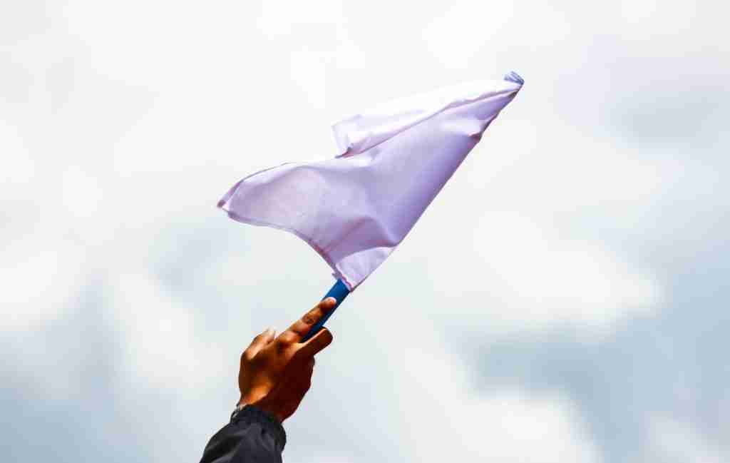 A hand holds up a white flag against a bright, cloudy sky, symbolizing surrender or calling for peace—an image that can resonate deeply with mixed neurotype couples navigating love accommodations and understanding each other’s slow processing speed.